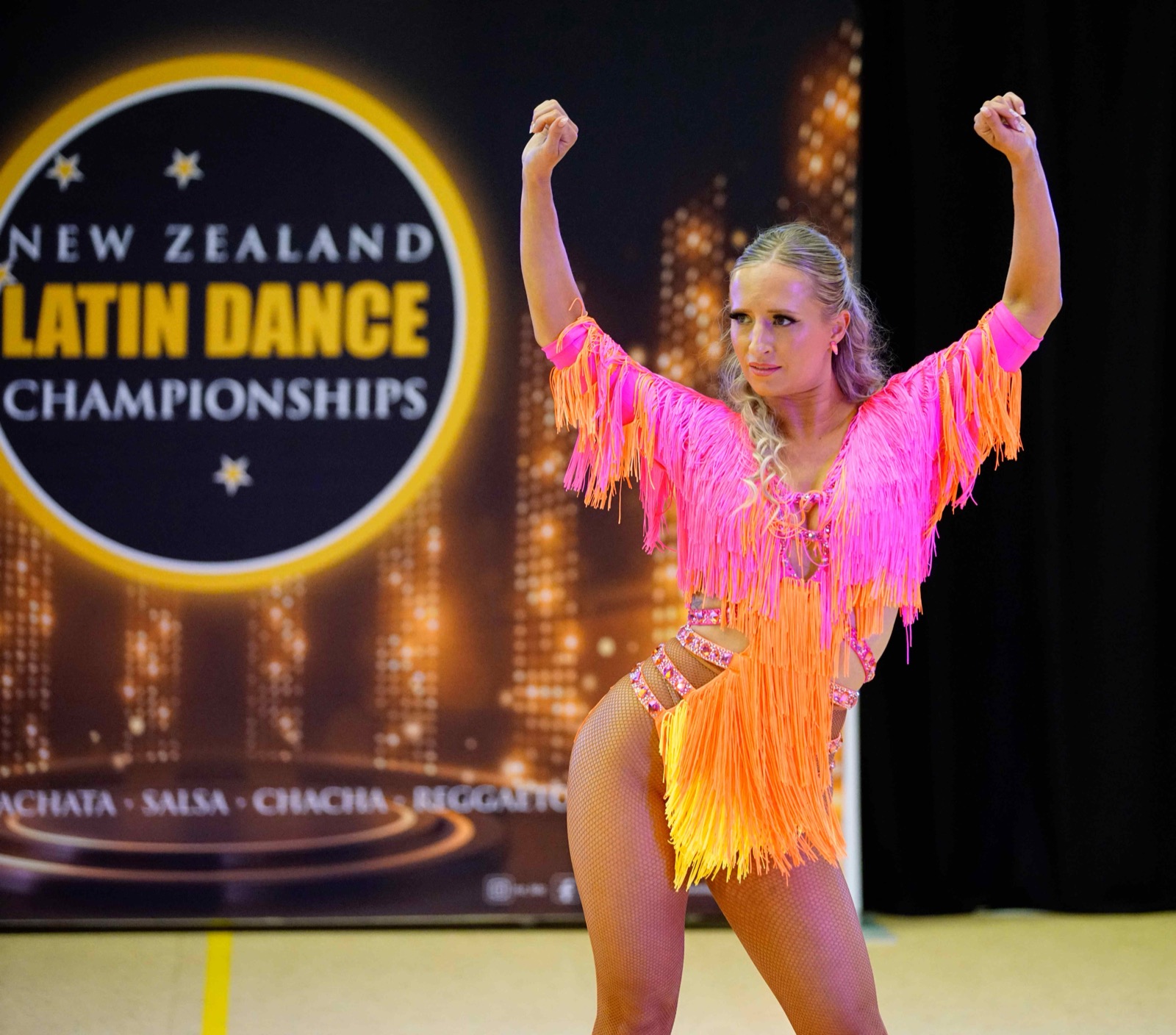 Soloist in a neon pink and orange fringed dress, arms raised